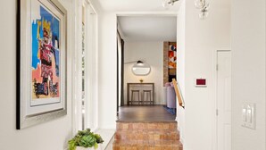 Un pasillo con una escalera que conduce a un comedor, una obra de arte enmarcada en la pared y una planta en maceta en el suelo.