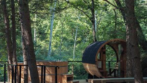 Une cabane en bois, de forme cylindrique, entourée d’arbres au cœur d’une forêt.