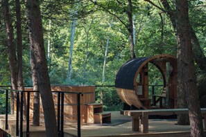 Eine Holzhütte mit einer tonnenförmigen Struktur, umgeben von Bäumen in einem Wald.
