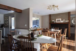 A dining area with a large round table, wooden chairs, and a fireplace.