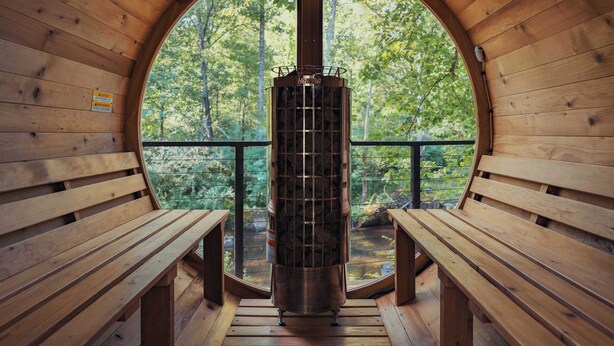 Une cabane en bois dotée d’une grande fenêtre circulaire, de bancs en bois et d’un poêle en métal placé au centre.