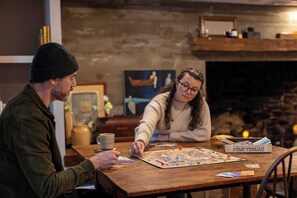 Two people playing a board game at a wooden table with a fireplace in the background.