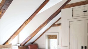 Une chambre avec un plafond en pente, un lit, un banc, une chaise et un tapis à motifs.