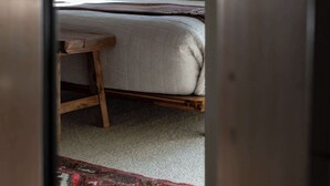 Une chambre avec un plafond en pente, un lit avec des oreillers, une chaise en bois et un tapis à motifs.
