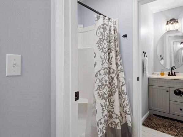 A bathroom with a shower curtain, a mirror, and a sink with a soap dispenser. - Jax Joint - Pet Friendly - perfect family vacation spot! (Crane Hill)