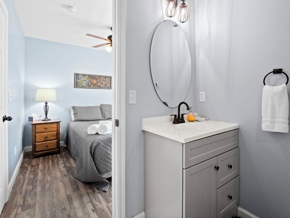 Een slaapkamer met een bed, nachtkastje, lamp en een schilderij aan de muur.