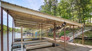 A wooden dock with a covered seating area, a small boat docked, and a bridge leading to a docked boat. - Jax Joint - Pet Friendly - perfect family vacation spot! (Crane Hill)