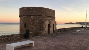 Un bâtiment en pierre doté d’une structure circulaire, d’un banc et offrant une vue sur la mer au coucher du soleil.