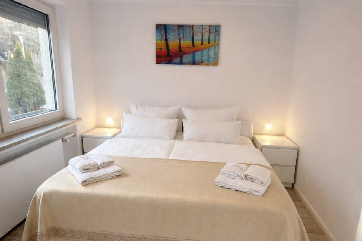 Ett sovrum med en stor säng, två sängbord, ett fönster och en tavla på väggen.