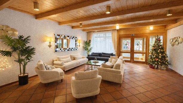 Ein geräumiges Wohnzimmer mit hoher Decke, Holzbalken, einem großen Fenster mit Vorhängen, einem Weihnachtsbaum und mehreren Sofas und Sesseln.