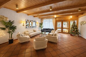 Ein geräumiges Wohnzimmer mit hoher Decke, Holzbalken, einem großen Fenster mit Vorhängen, einem Weihnachtsbaum und mehreren Sofas und Sesseln.