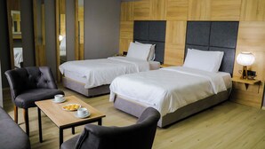Una camera d'albergo con due letti singoli, una testiera in legno, un tavolino con una tazza e un piattino di biscotti, e una sedia.