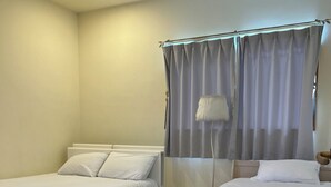 A bedroom with two single beds, a bedside table with a lamp, and a window with curtains. - Spacious detached house with BBQ and 1 minute walk to the ocean* 4LDK with 4 parking spaces*. (北中城村美崎)