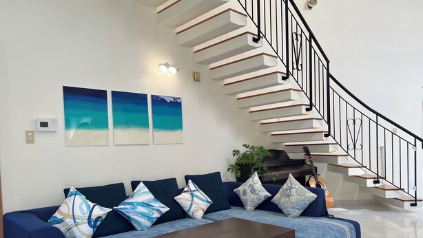 A modern living room with a dark blue sofa, a wooden coffee table, and a staircase with black railings. - Spacious detached house with BBQ and 1 minute walk to the ocean* 4LDK with 4 parking spaces*. (北中城村美崎)