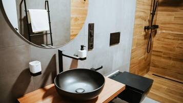 A modern bathroom with a wooden vanity, a black basin, a mirror, a towel rack, and a shower area.