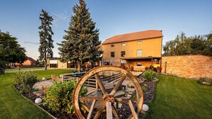 A building with a large water wheel in the garden, surrounded by well-maintained grass and plants. - Galerie mlýn Žeraviny (Žeraviny)