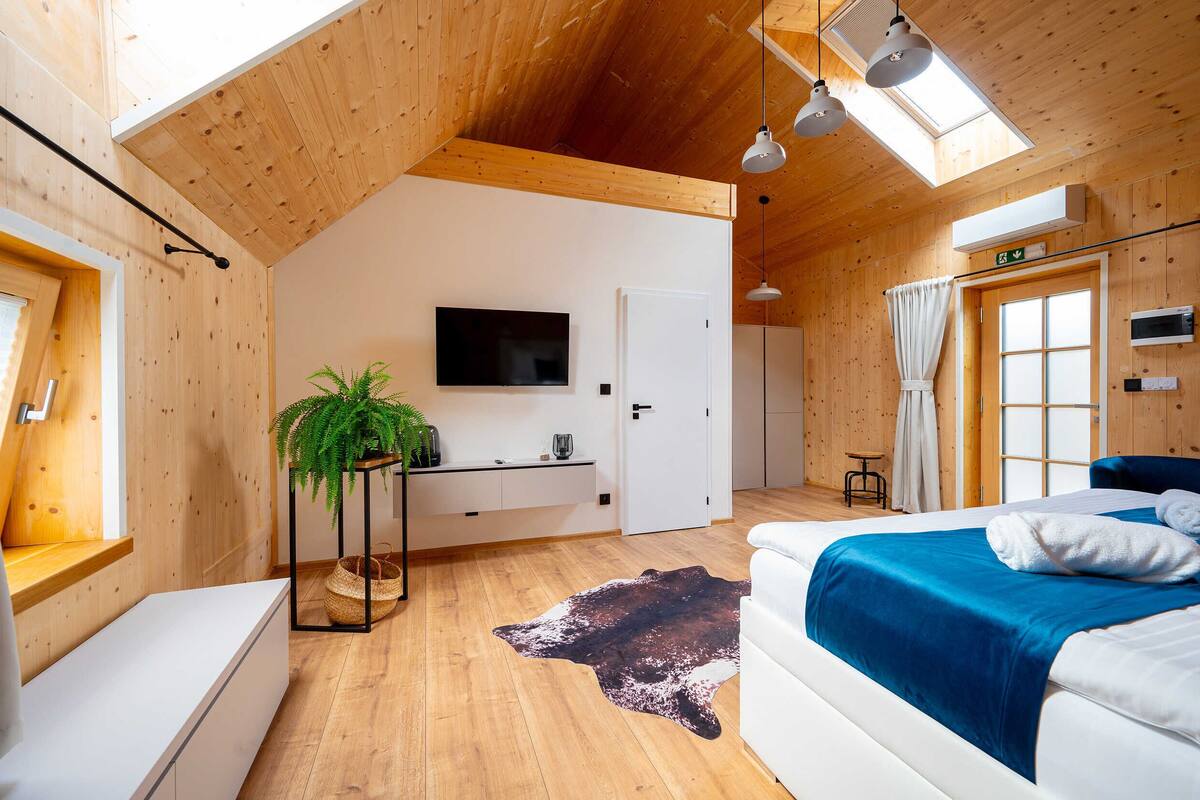 A modern bedroom with a wooden ceiling, a mounted TV, a bed with blue bedding, a cowhide rug, and a small plant.