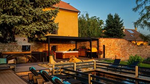 A pool area with lounge chairs and a hot tub, surrounded by a wooden deck and stone walls. - Galerie mlýn Žeraviny (Žeraviny)