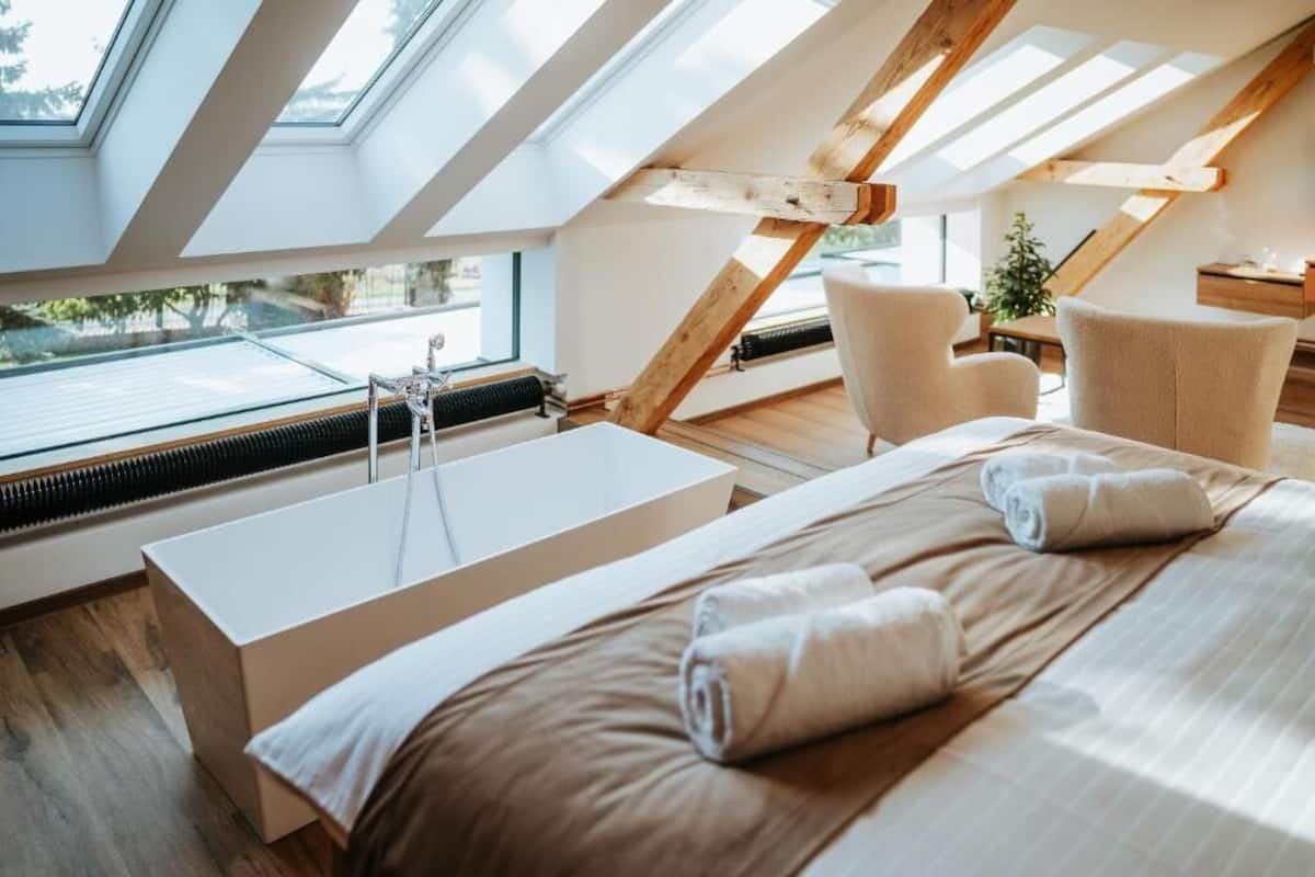 A modern bedroom with a skylight, a large bed, a bathtub, and a seating area.