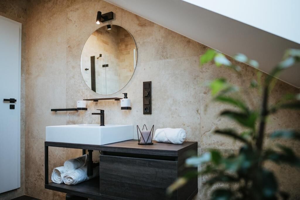 A modern bathroom with a large round mirror, a white sink, and a dark wooden vanity.