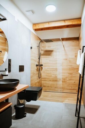 Une salle de bain moderne avec un plancher en bois, un grand miroir, un lavabo noir et un espace douche.