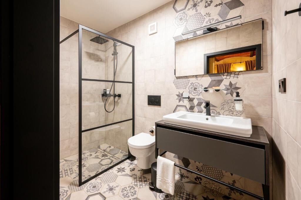 Een moderne badkamer met een douchecabine van glas, een witte wastafel en betegelde vloeren.
