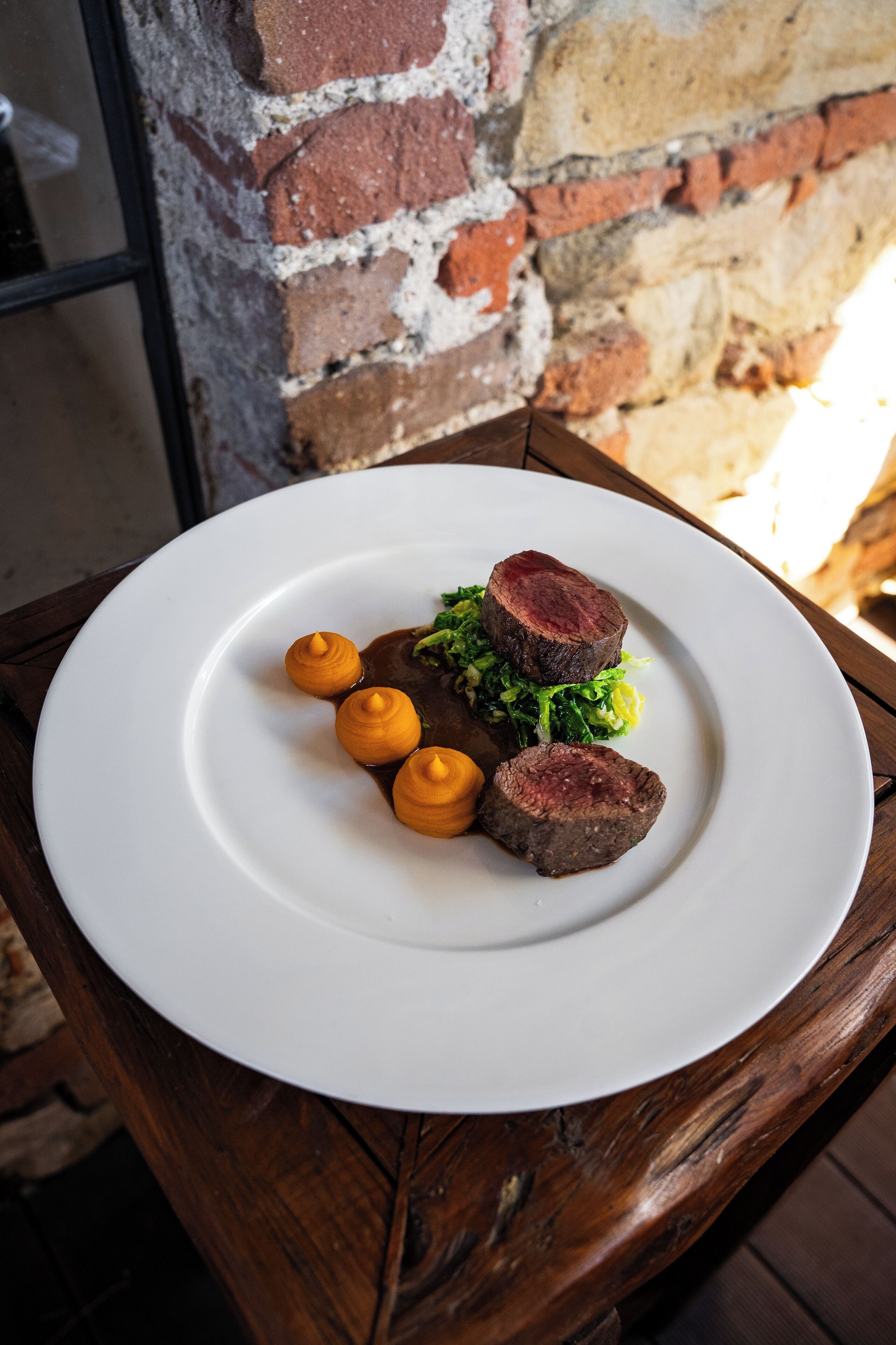 Un plato blanco con un filete y verduras sobre una mesa de madera.