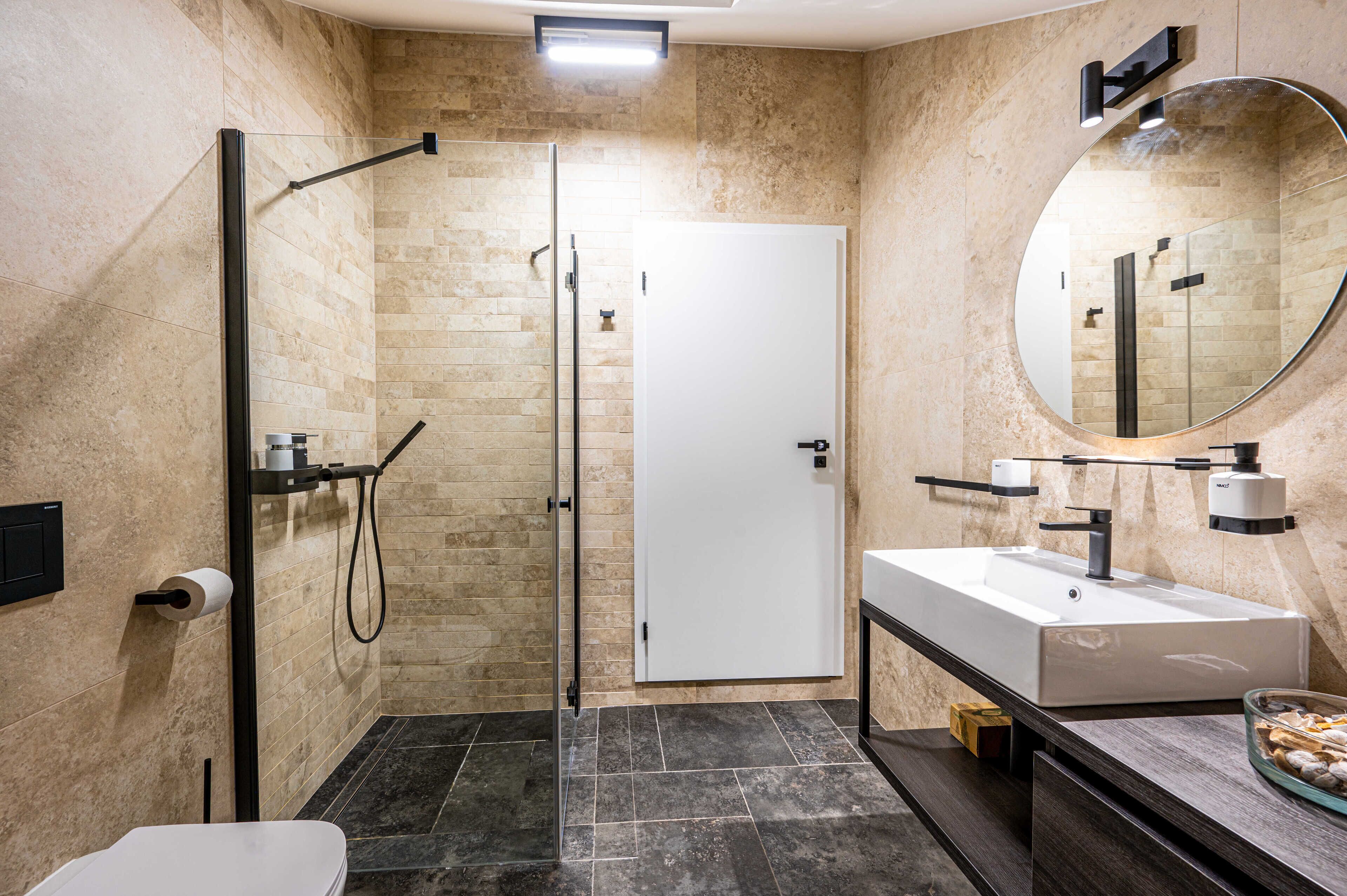 A modern bathroom with a glass-enclosed shower, a white sink, and a large mirror.
