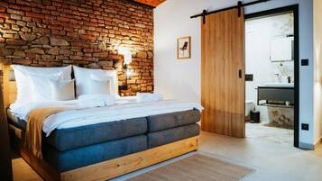 Un dormitorio con pared de ladrillo, estructura de cama de madera, puerta corredera y baño visible a través de la puerta.