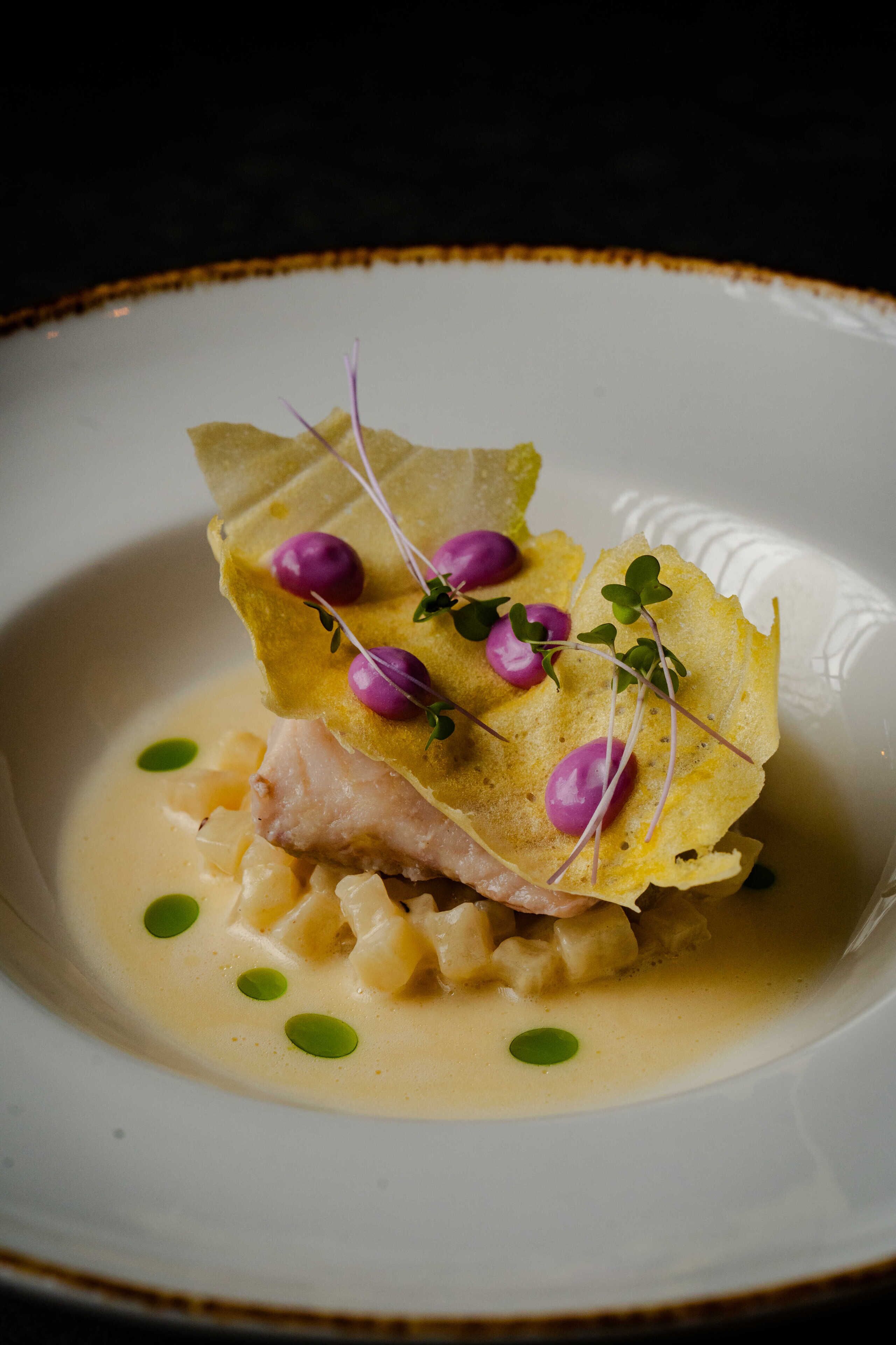 A plate of food with a creamy sauce, green garnish, and a piece of fish.