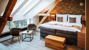 A modern loft bedroom with a sloped ceiling, a stone wall, a large bed, and a skylight. - Galerie mlýn Žeraviny (Žeraviny)
