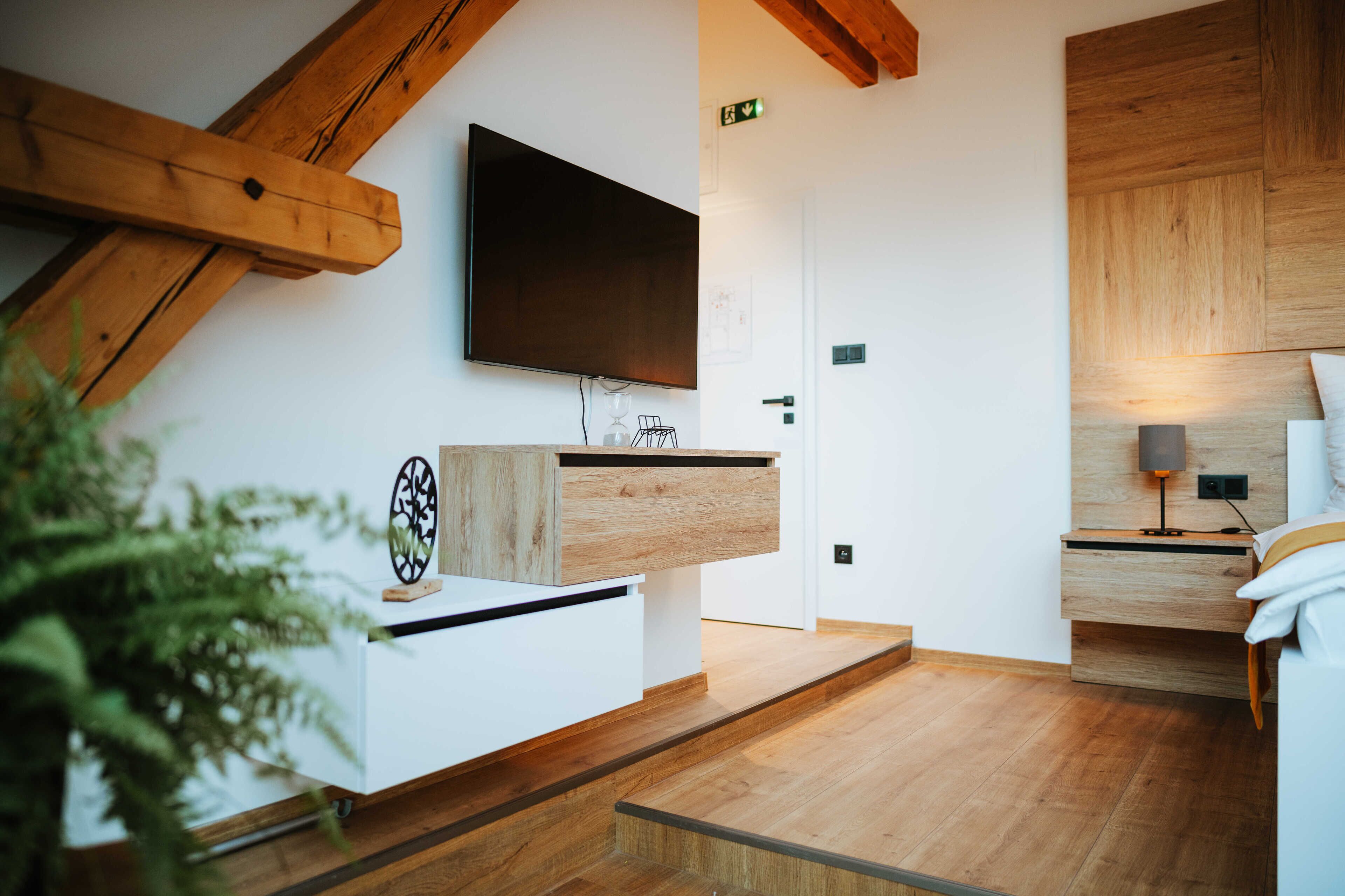 A modern room with a wooden ceiling, a mounted TV, a wooden cabinet, and a bed with a bedside table.