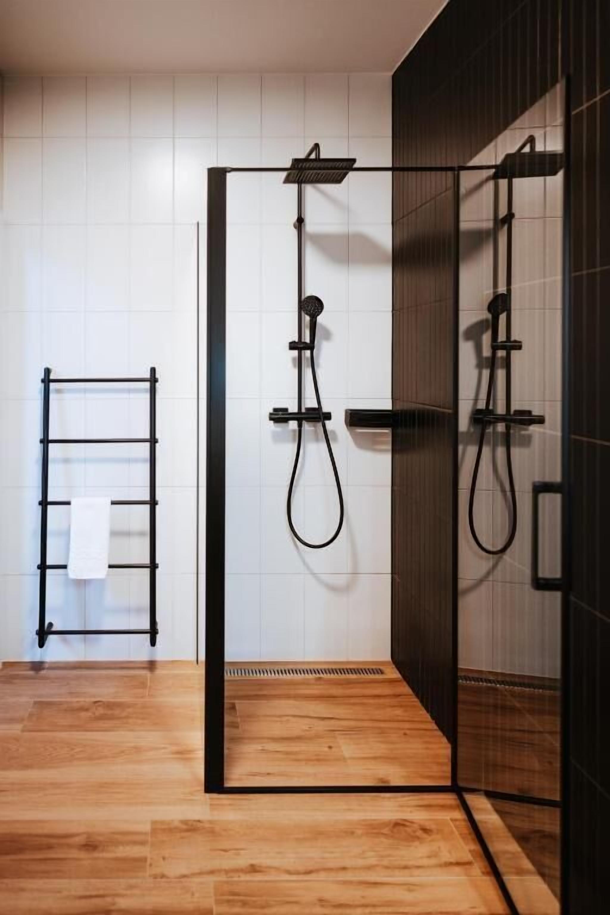 A modern bathroom with a glass-enclosed shower, a black towel rack, and a wooden floor.