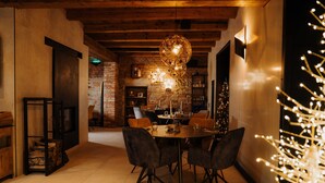 A dining area with a brick wall, wooden ceiling, and a chandelier. There is a Christmas tree with lights on the right. - Galerie mlýn Žeraviny (Žeraviny)