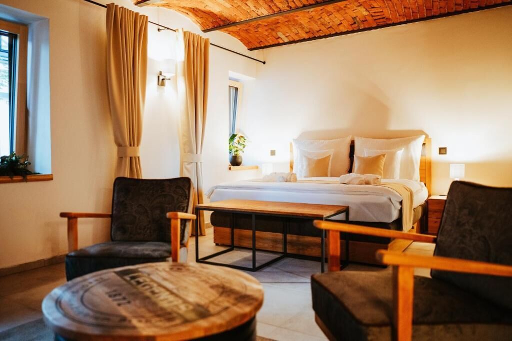 A cozy room with a bed, two chairs, a small table, and a window with curtains.
