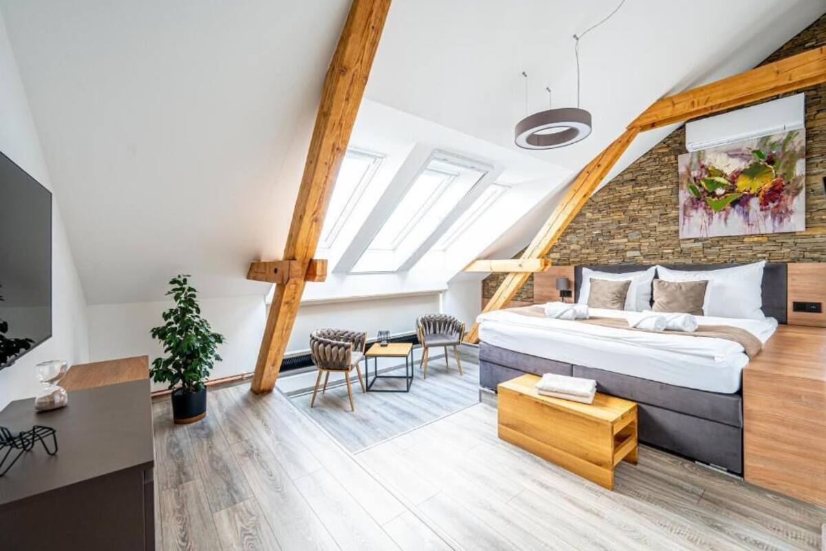A modern loft bedroom with a sloped ceiling, skylights, a bed, a desk, and a potted plant.