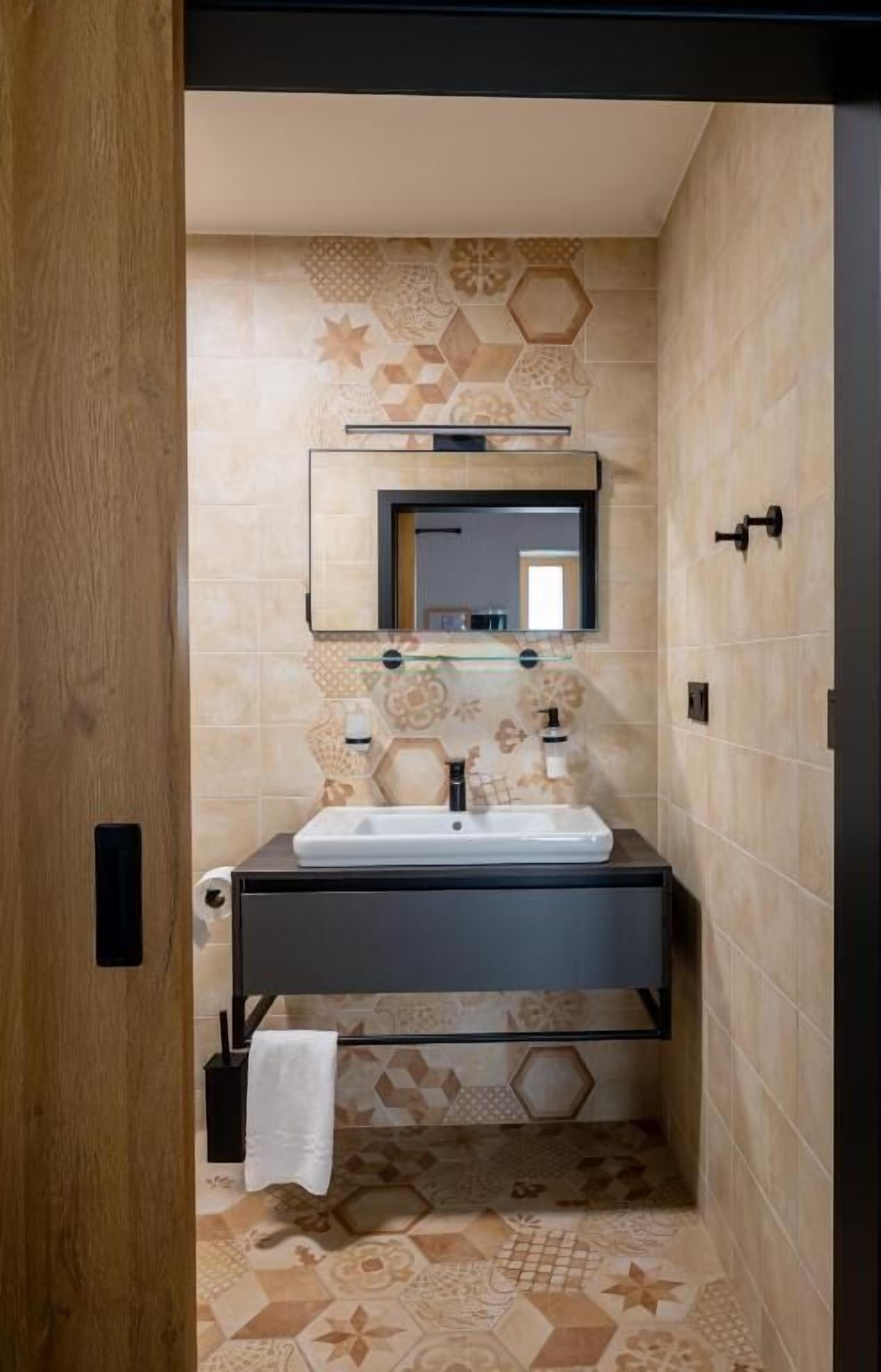 A bathroom with a sink, mirror, and patterned tiles.