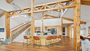 Una cocina amplia con vigas de madera, una isla central con taburetes altos y una escalera que sube a un nivel superior.