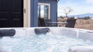 Un jacuzzi con agua salpicando, un edificio azul con una puerta y una ventana, y una mesa con sillas afuera.