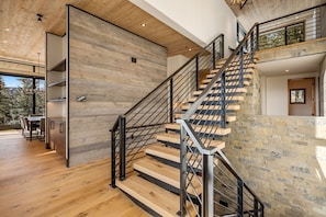 A modern interior with a wooden staircase, a dining area, and a view of trees outside. - Big Sky View  - Property In Big Sky (Big Sky)