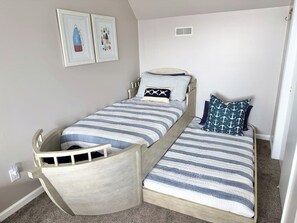 A single bed with a wooden frame and a striped bedspread, a bedside table, and two framed pictures on the wall. - Waterfront Private Beach byCountry Road Properties (Lower Township)