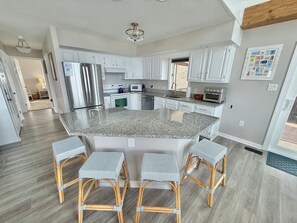 A modern kitchen with white cabinets, a granite countertop, and a central island with bar stools. - Waterfront Private Beach byCountry Road Properties (Lower Township)