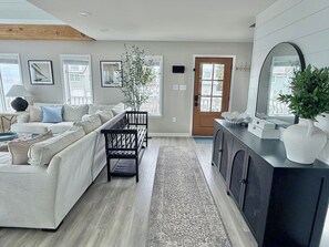 A modern living room with a sectional sofa, a black bench, a console table with decorative items, and a large mirror. - Waterfront Private Beach byCountry Road Properties (Lower Township)