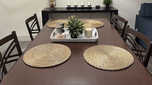 Un comedor con una mesa marrón, individuales tejidos, velas, un reloj y una planta pequeña.