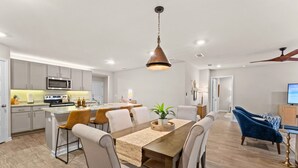 A modern kitchen with a microwave, stove, and dining area with a wooden table and chairs. - Family-Friendly Retreat Near Gulf Shores, Beach (Foley)