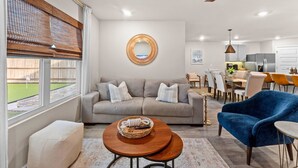 A modern living room with a sofa, a blue armchair, a round coffee table, and a dining area in the background. - Family-Friendly Retreat Near Gulf Shores, Beach (Foley)
