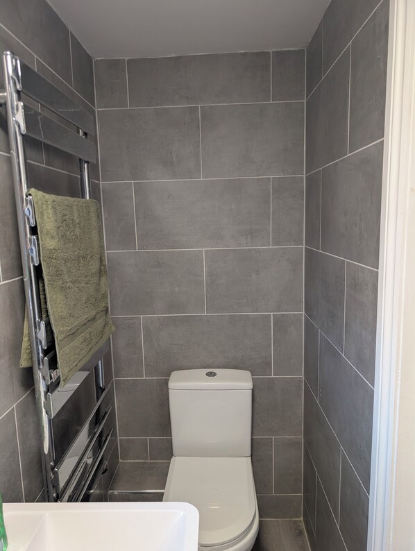 A small bathroom with a toilet, a towel rack with a green towel, and tiled walls.
