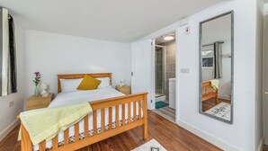 A bedroom with a wooden bed, a nightstand, a mirror, and a door leading to a bathroom. - Self-Contained Flat in Didcot near Shops, Milton Park, Harwell & Station (Didcot)
