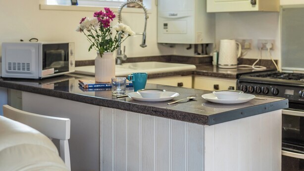 A kitchen with a central island, a microwave, a sink, a stove, and a vase with flowers. - Self-Contained Flat in Didcot near Shops, Milton Park, Harwell & Station (Didcot)