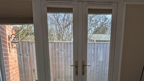 A bedroom with a bed, a wooden bench, a window with a view of a backyard, and a door. - Self-Contained Flat in Didcot near Shops, Milton Park, Harwell & Station (Didcot)